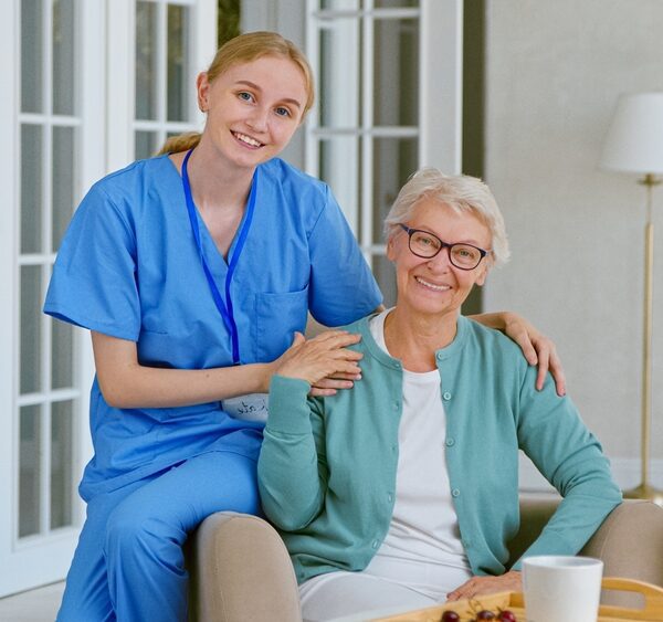 Smiling,Young,Blonde,Nurse,In,Uniform,Takes,Care,Of,Senior